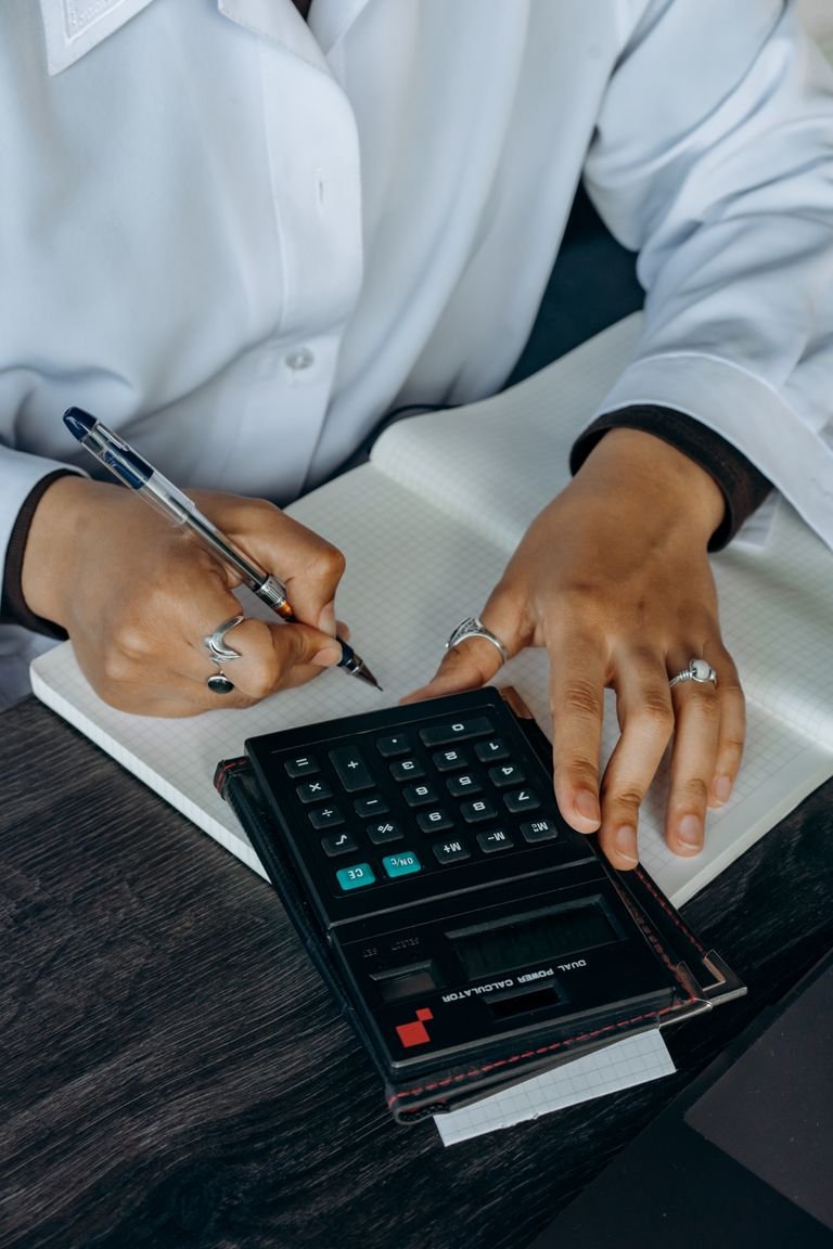 Close-up of hands writing in a notebook while using a calculator. Ideal for finance and business concepts.